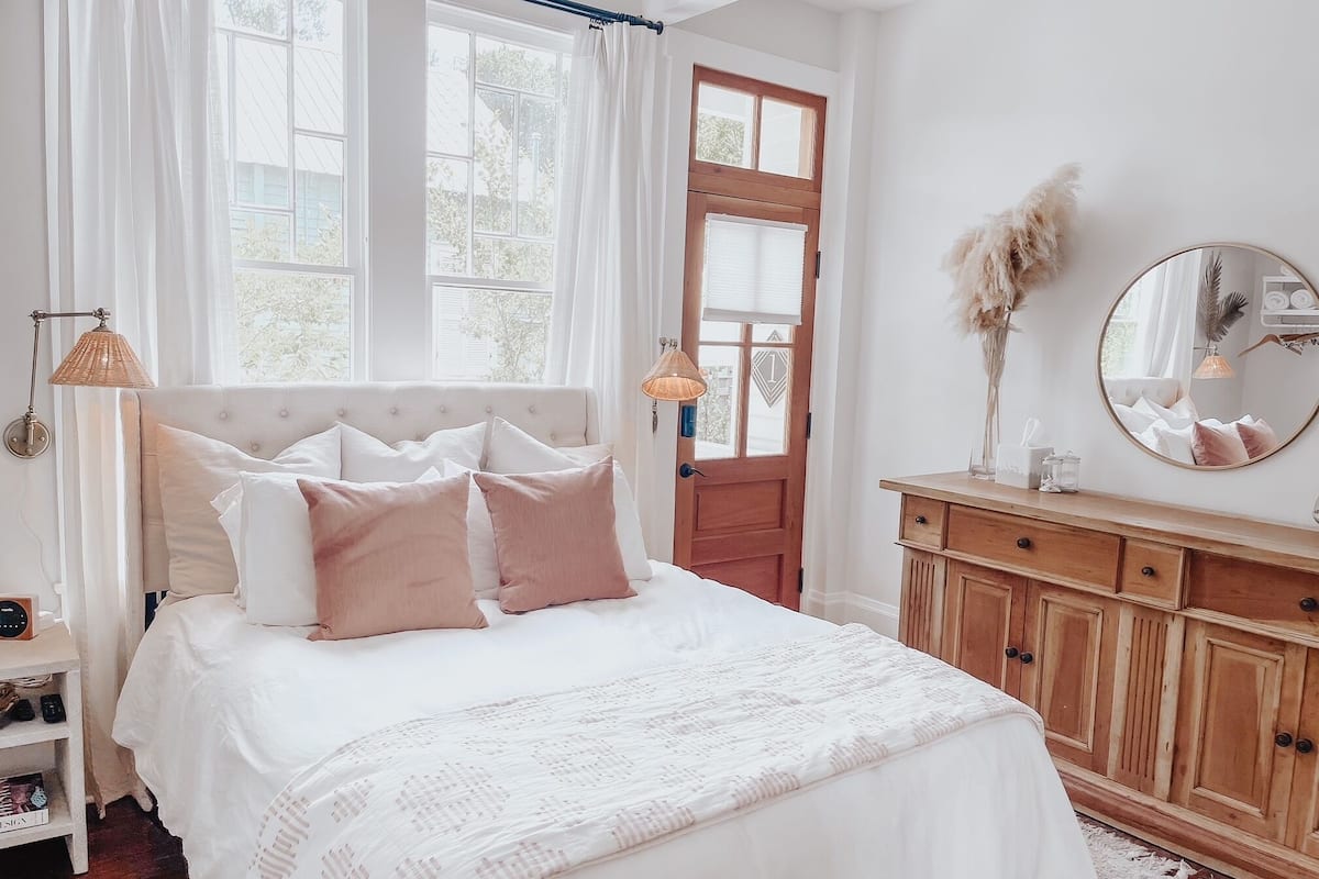 A bedroom with a large bed, a wooden dresser, a mirror, and two windows with curtains.
