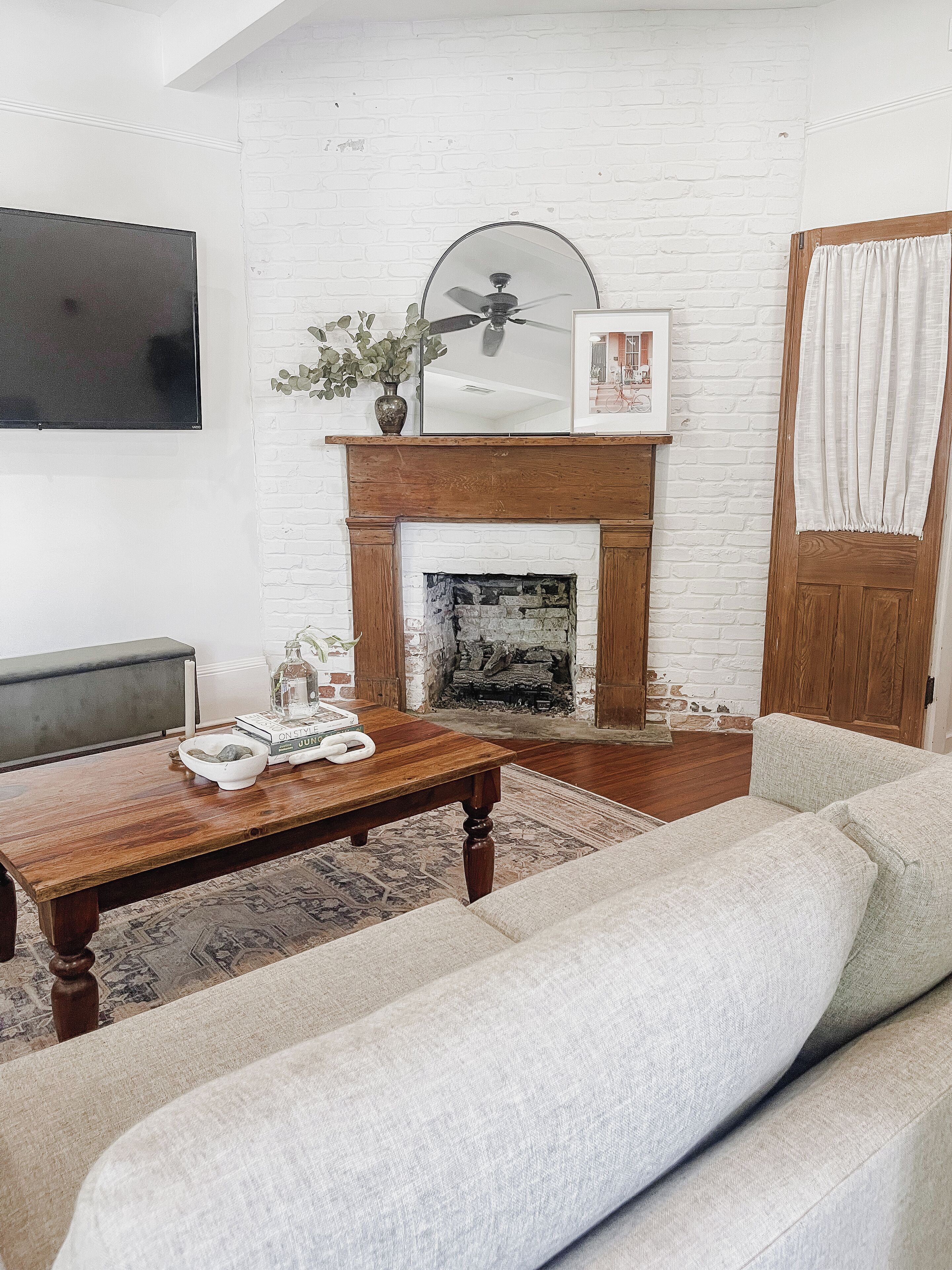 A living room with a fireplace, a flat-screen TV mounted on the wall, a wooden coffee table, and a grey sofa.