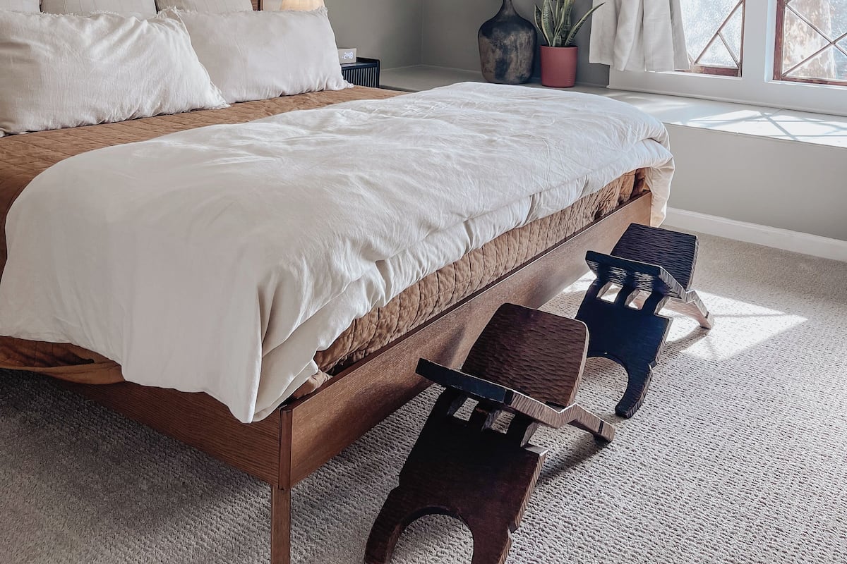 A bedroom with a sloped ceiling, a large bed, a bedside table, a potted plant, and a window with curtains.