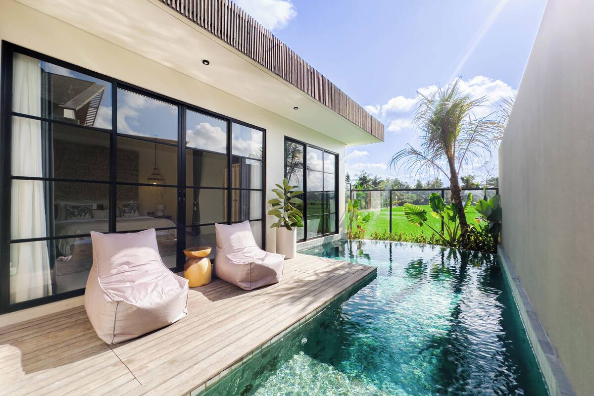 A modern poolside area with a wooden deck, large windows, and a view of a green landscape.