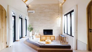 A spacious living area with a large TV, wooden furniture, and a stone wall.