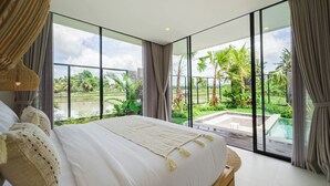 A modern bedroom with a large bed, a view of a swimming pool, and a lush garden.