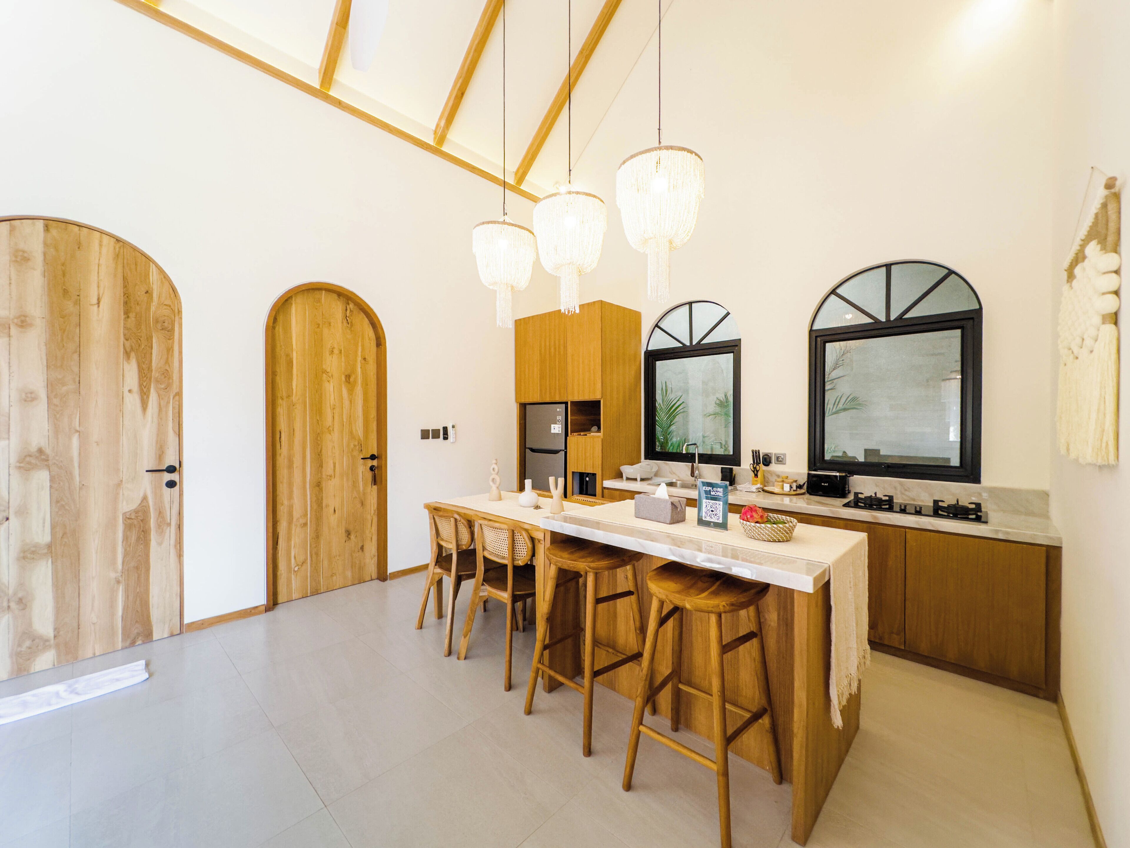 A modern kitchen with wooden cabinetry, a central island with stools, pendant lighting, and a large window with a view.