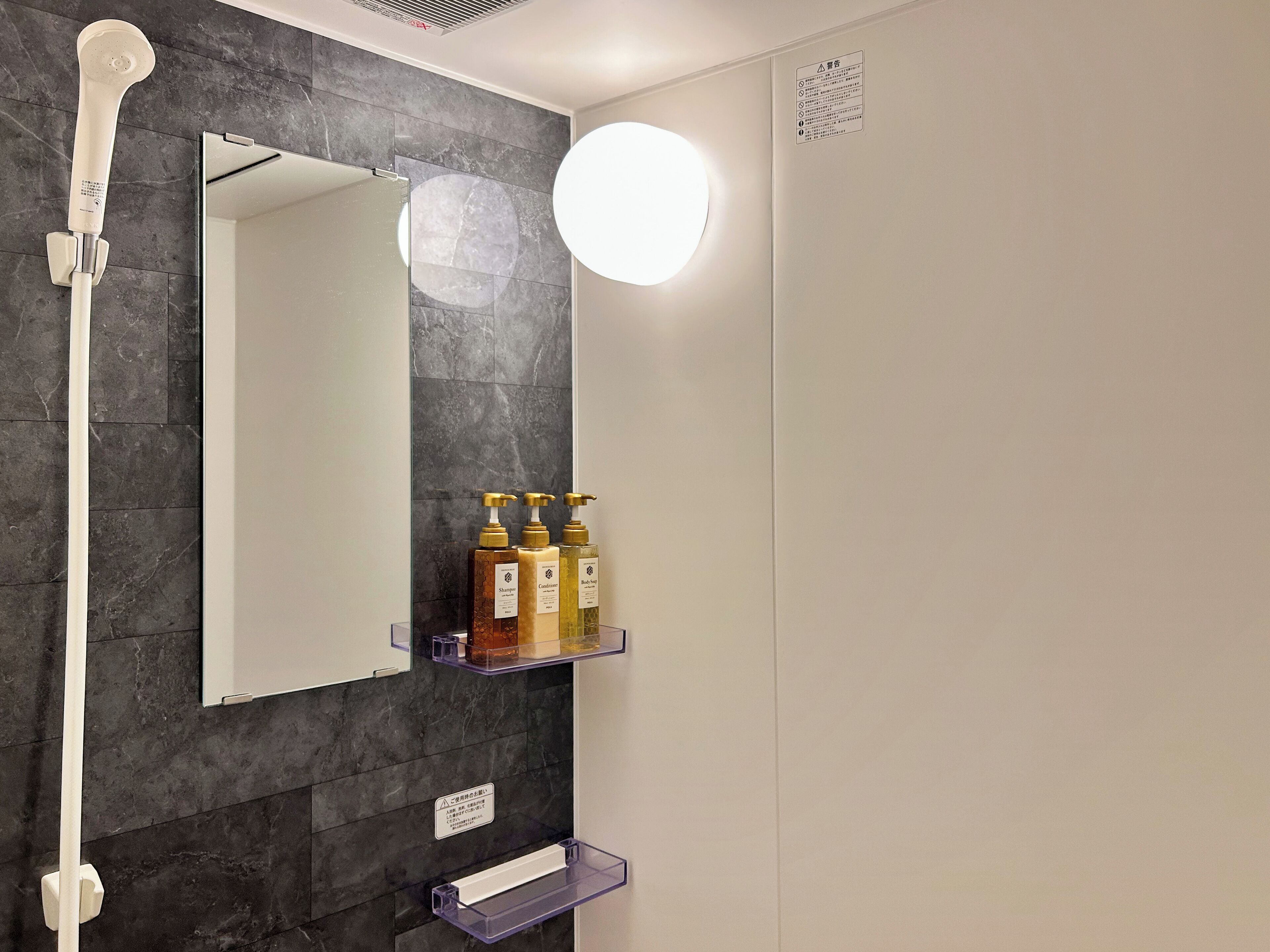 Un baño con ducha, espejo y repisas con artículos de aseo.