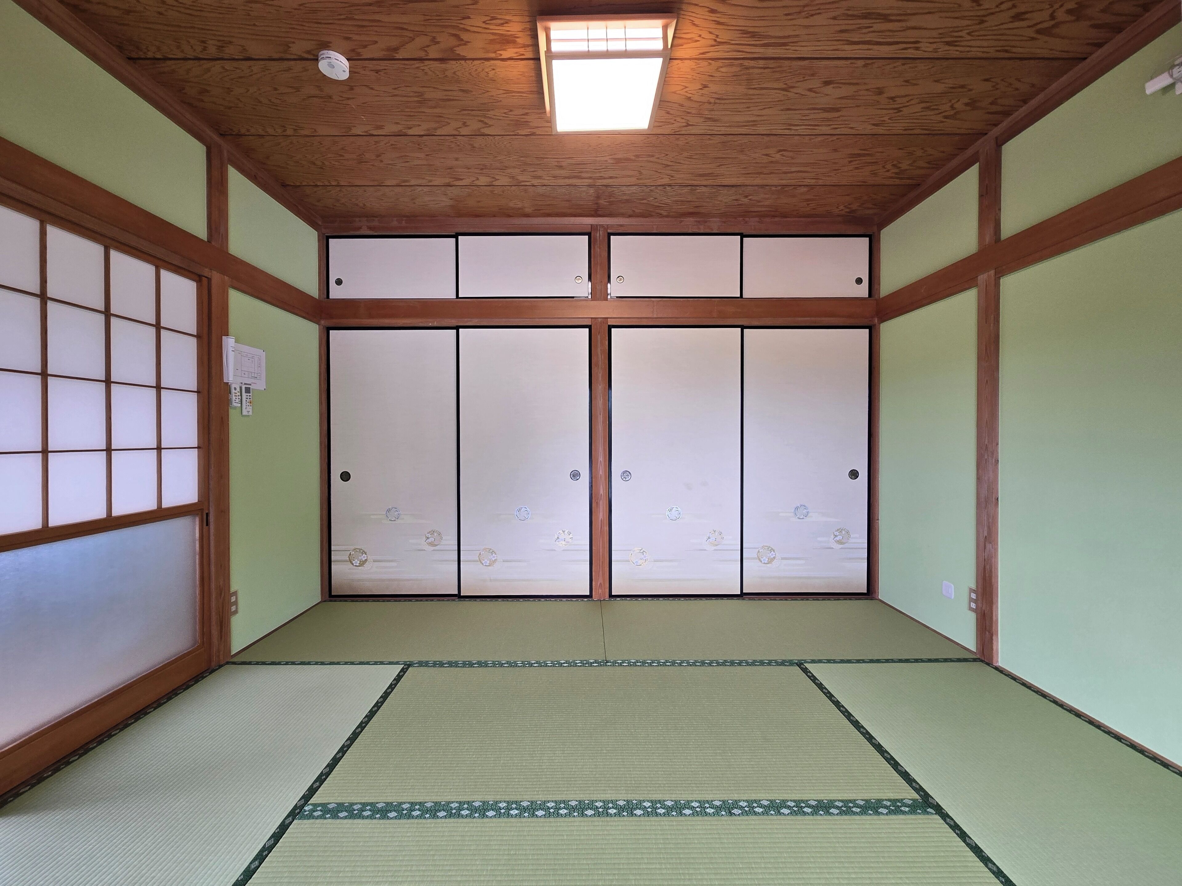 A traditional Japanese room with tatami flooring, sliding shoji doors, and a wooden ceiling.