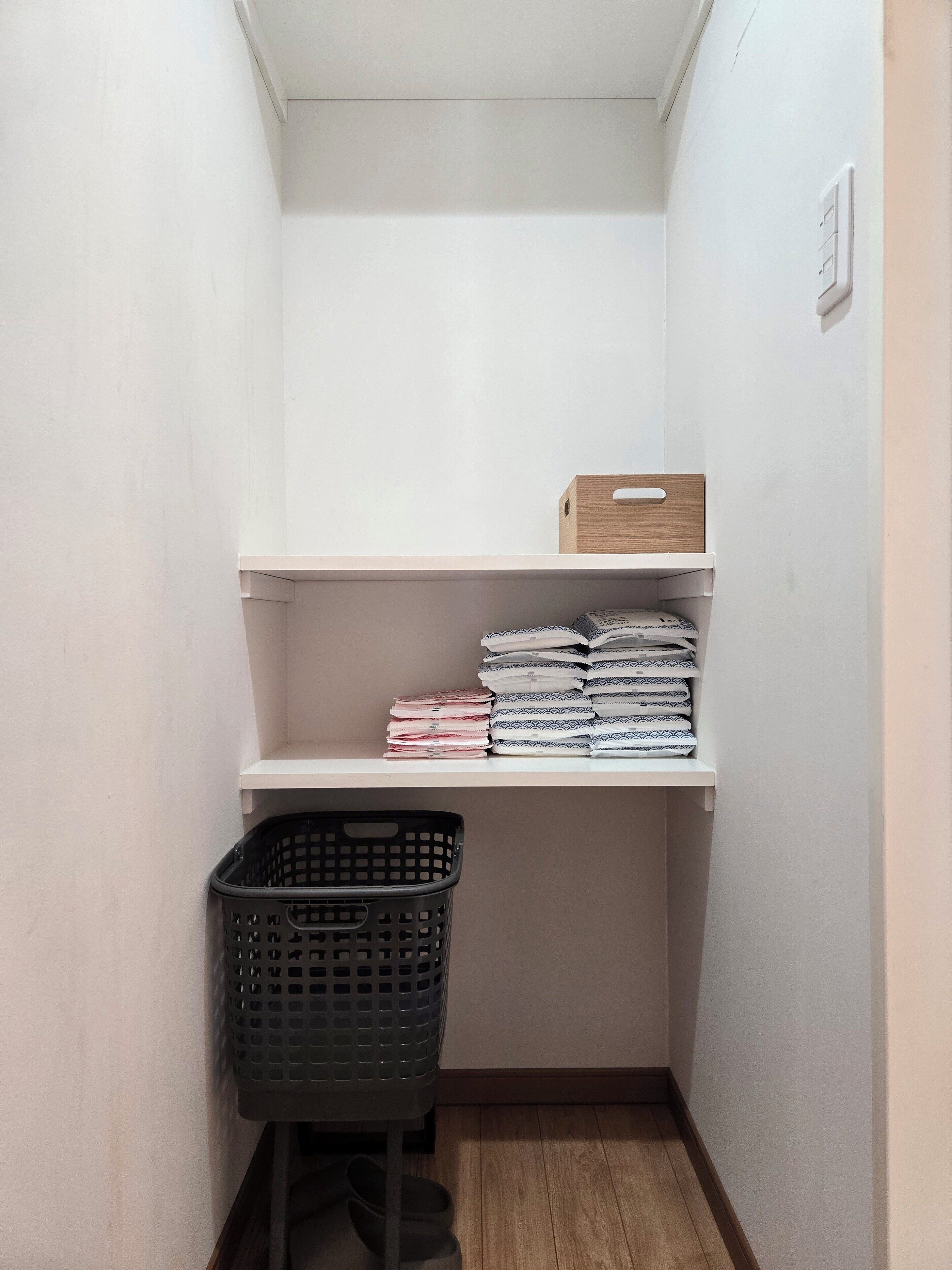 A small, organized closet with shelves for folded clothes and a basket for laundry.