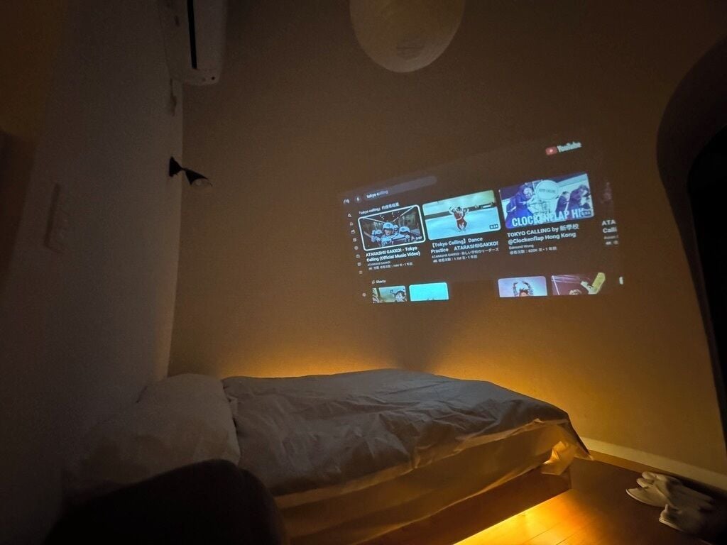 Une pièce comprenant un lit, un projecteur fixé au mur qui diffuse du contenu, et un ventilateur de plafond.