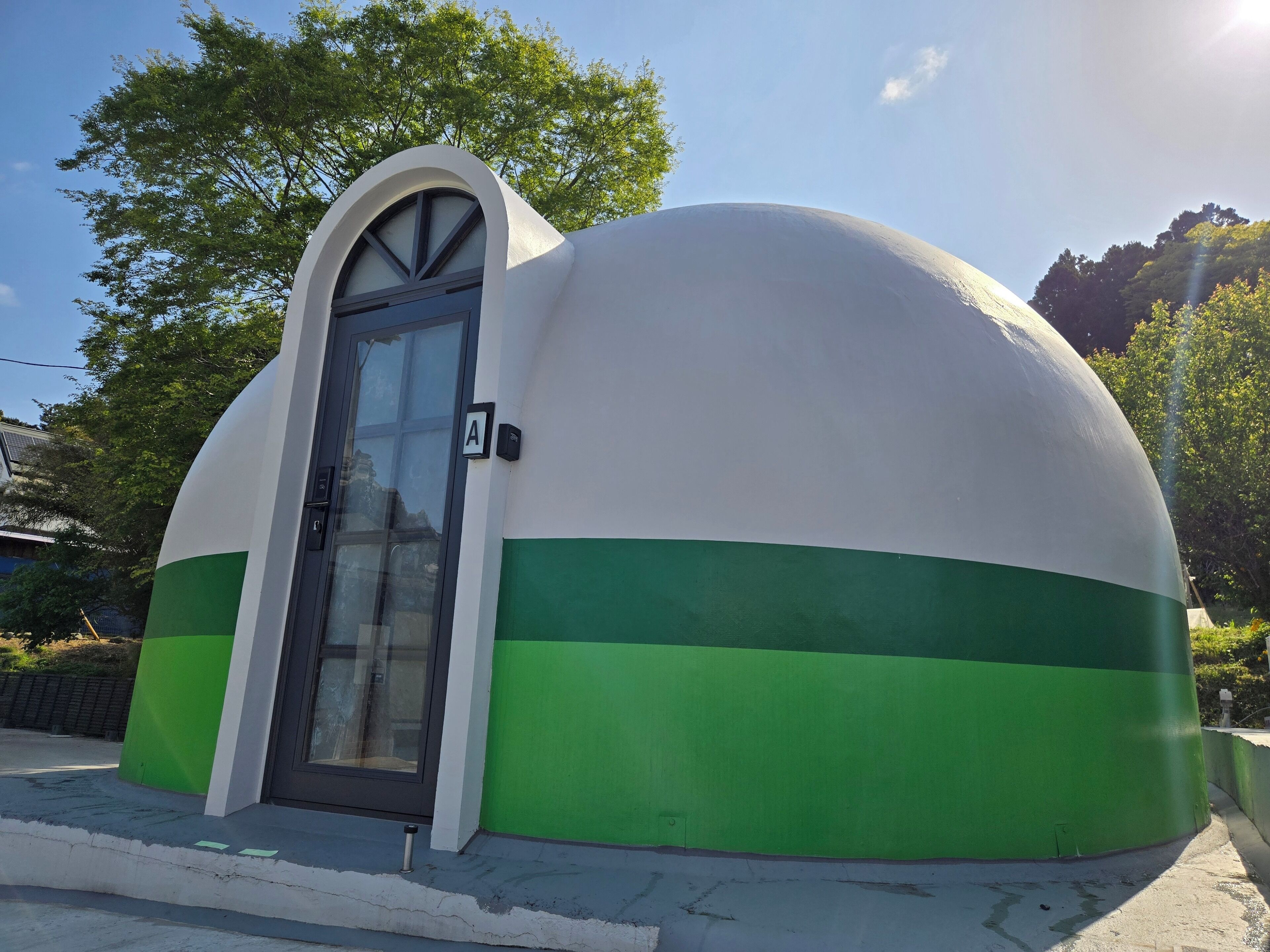 A dome-shaped building with a green and white color scheme, a door, and a small sign.