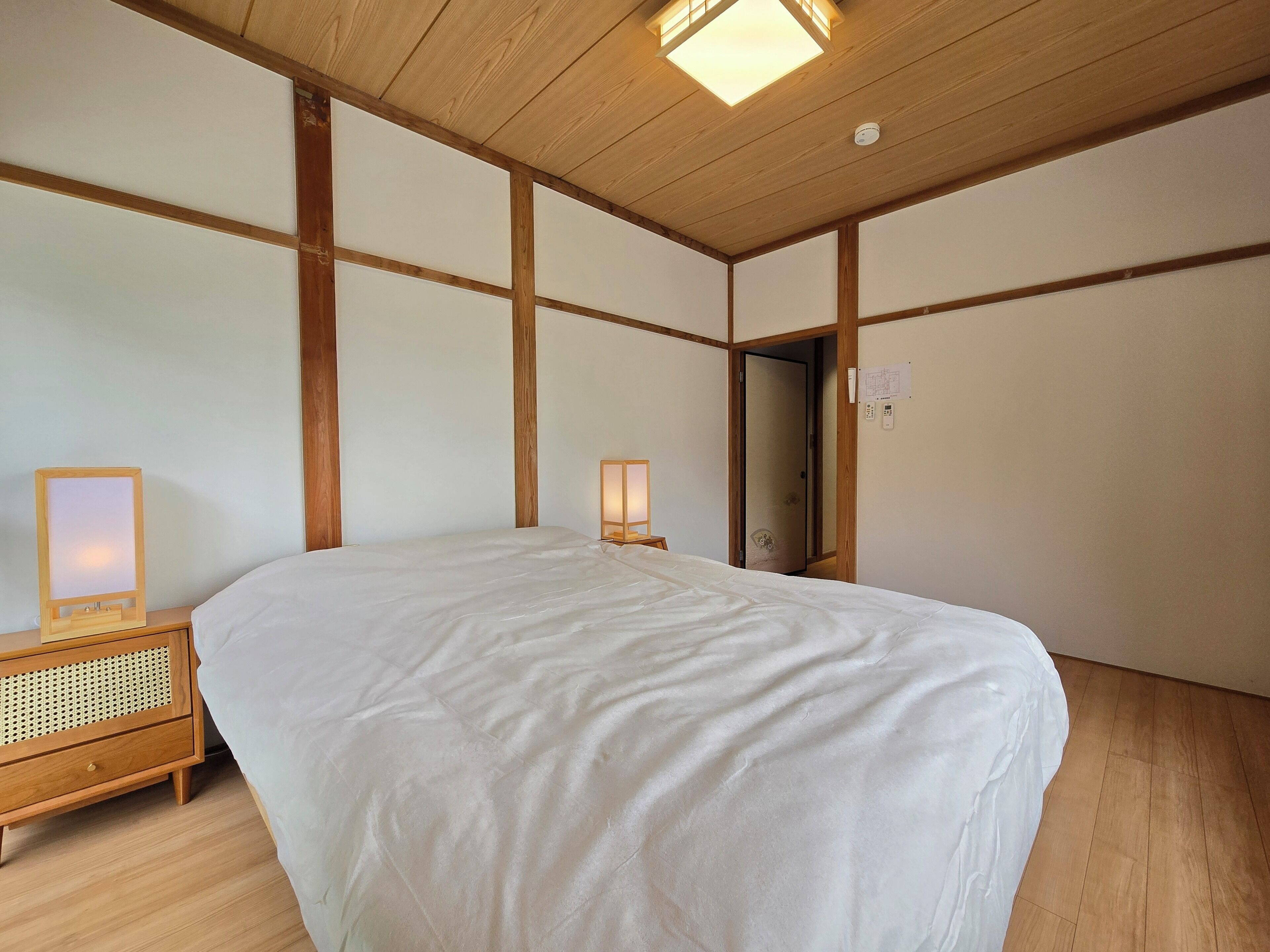 A bedroom with a large bed, wooden headboard, bedside tables with lamps, and a wooden ceiling.