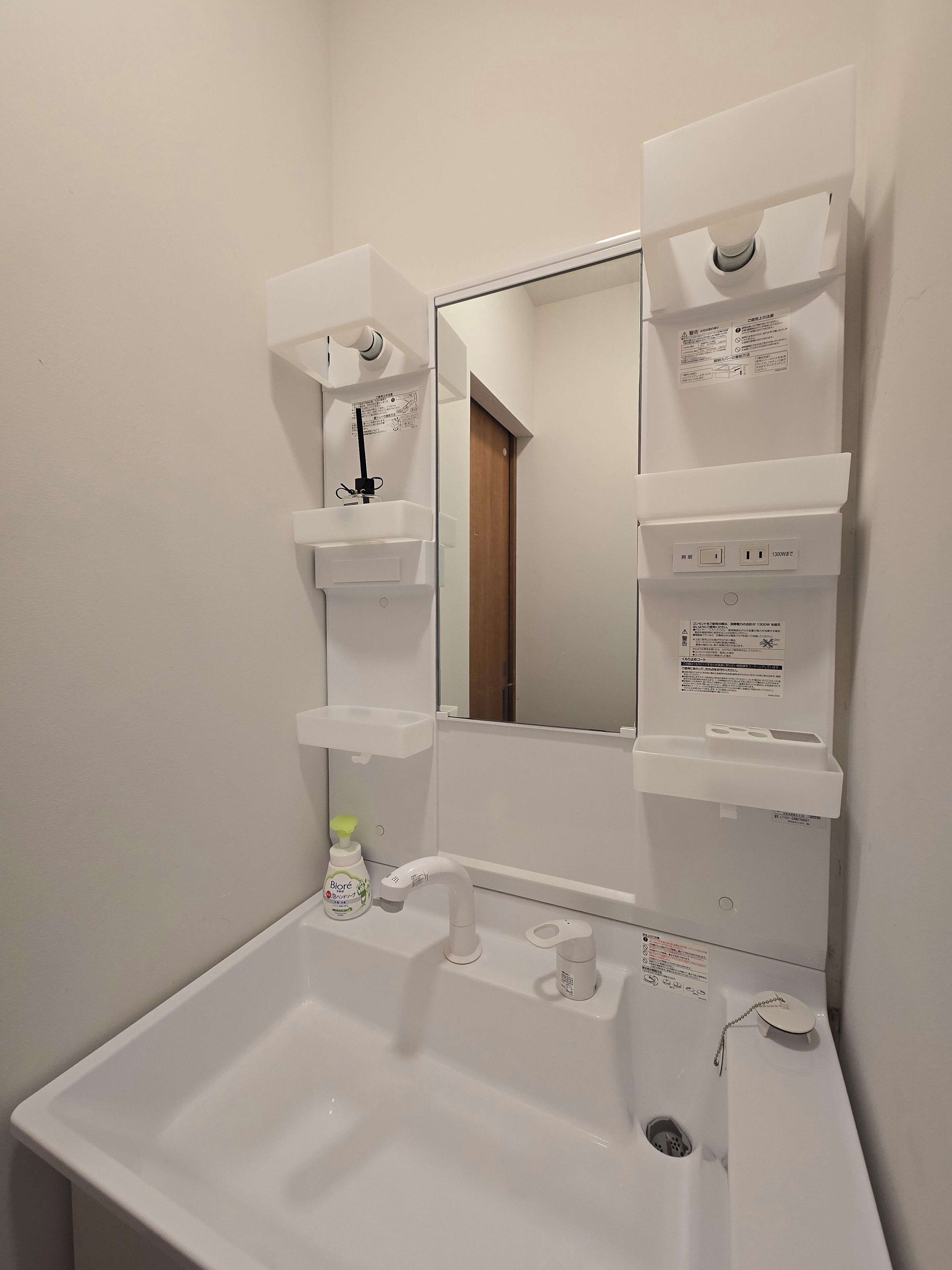 Un baño con lavamanos blanco, espejo y estantes.