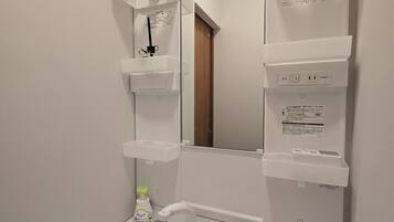 Un baño con lavamanos blanco, espejo y estantes.