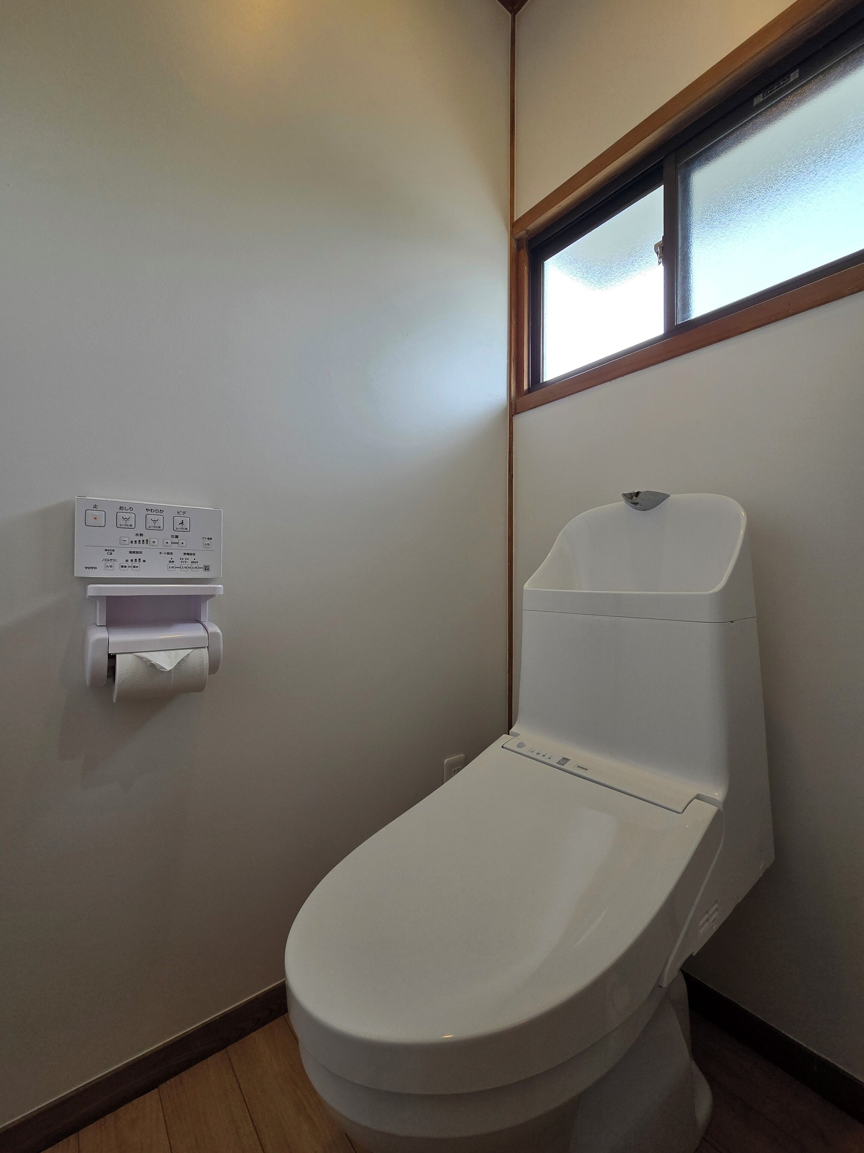 Ein kleines, sauberes Badezimmer mit Toilette, Papierhandtuchspender und einem Fenster über der Toilette.