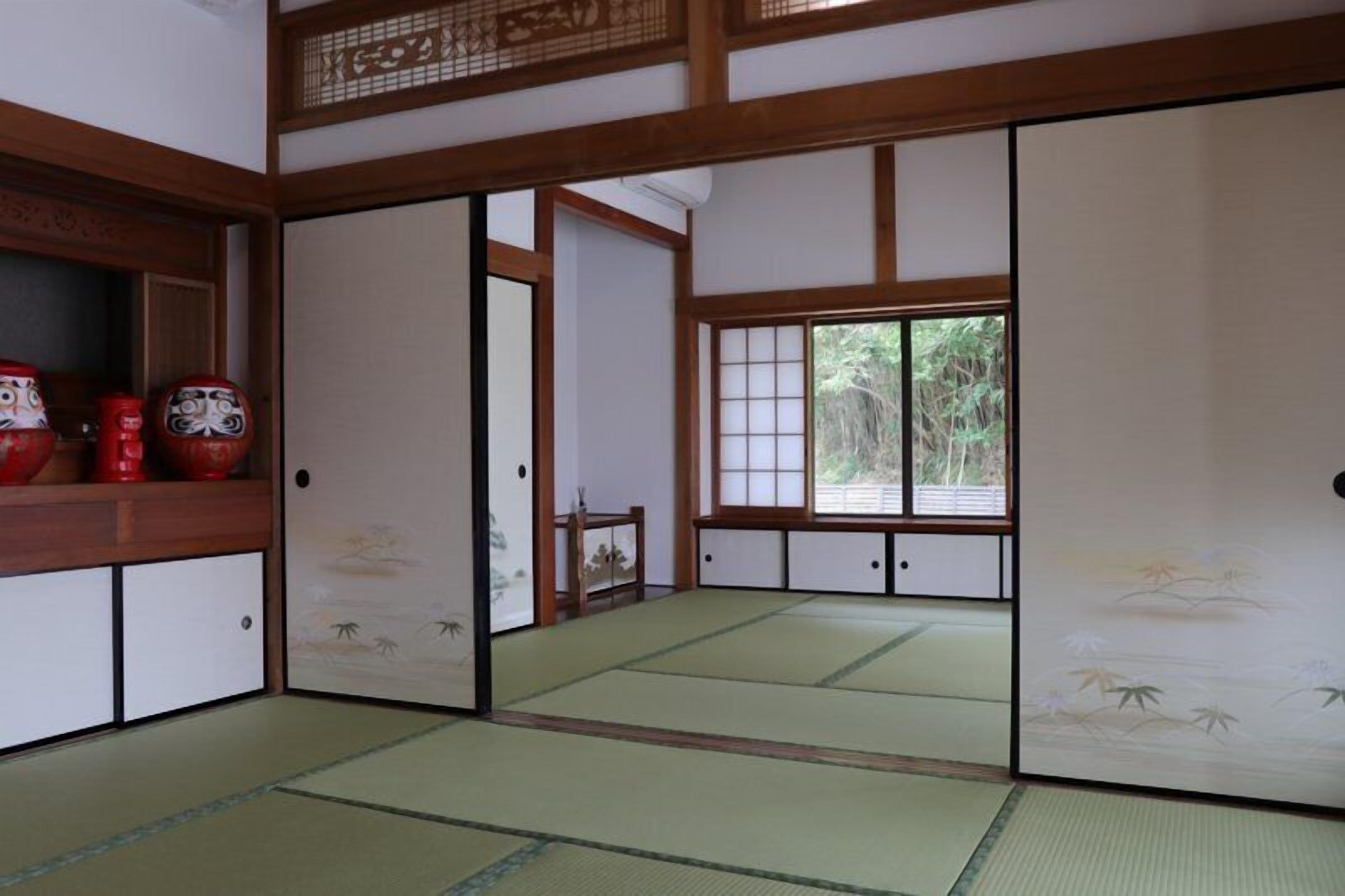 Una habitación japonesa tradicional con suelo de tatami, puertas correderas y vistas al verdor exterior.