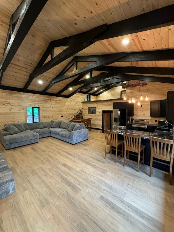 Amplia sala de estar con un sofá seccional grande, un comedor con sillas de madera y una cocina con electrodomésticos modernos.