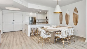 Una cocina moderna con armarios blancos, una isla central y un comedor con sillas de mimbre.