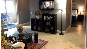 Un saló amb una televisió, un moble de divuité negre, un vas amb flors i una catifa estampada.