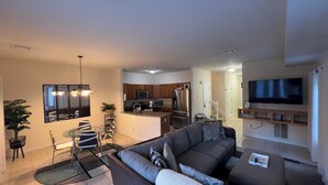 A modern living room with a sofa, dining table, and chairs. There is a kitchen area with appliances and a TV mounted on the wall. -  Charming 3 bedroom home Centrally located in Worcester (Worcester)