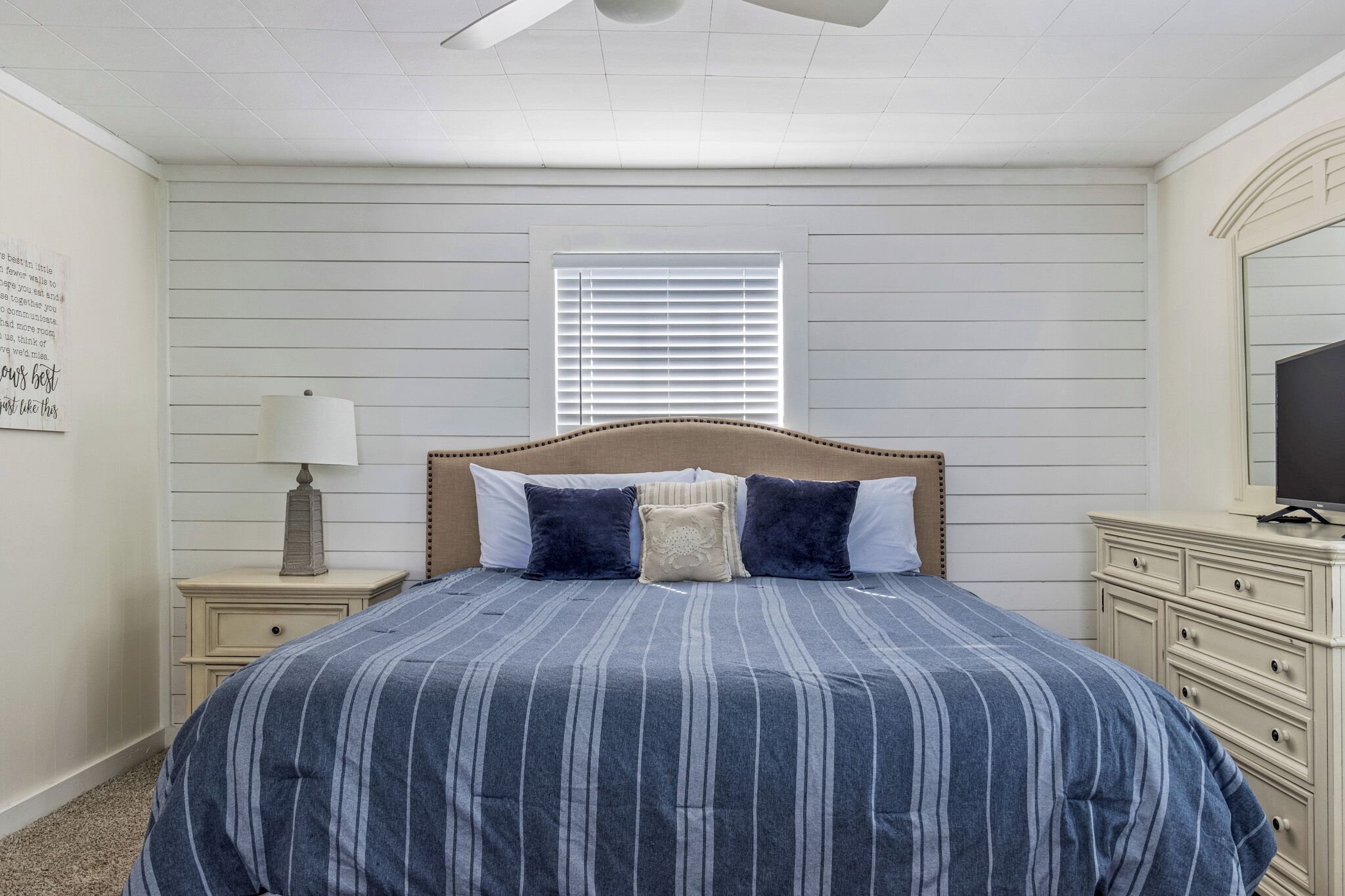 Un dormitorio con cama, mesitas de noche, lámpara, cómoda y ventana con persianas.