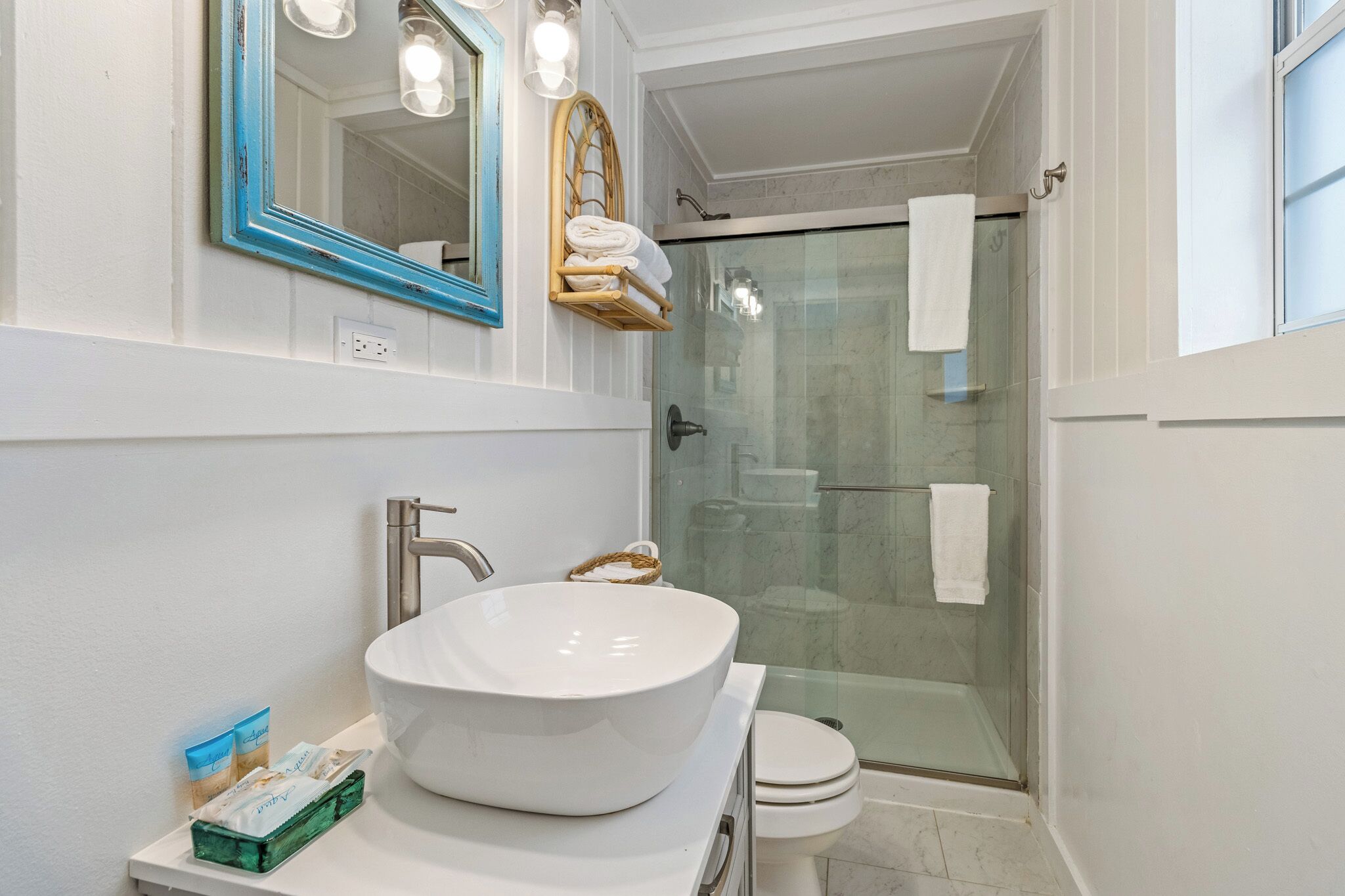 A bathroom with a large white sink, a mirror with a blue frame, a glass shower enclosure, and a white toilet.