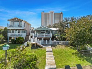 A coastal property with a wooden deck, a small garden, and a white picket fence. - Serenity Shores – 1 Block from Beach, Pet-Friendly! (Gulf Shores)