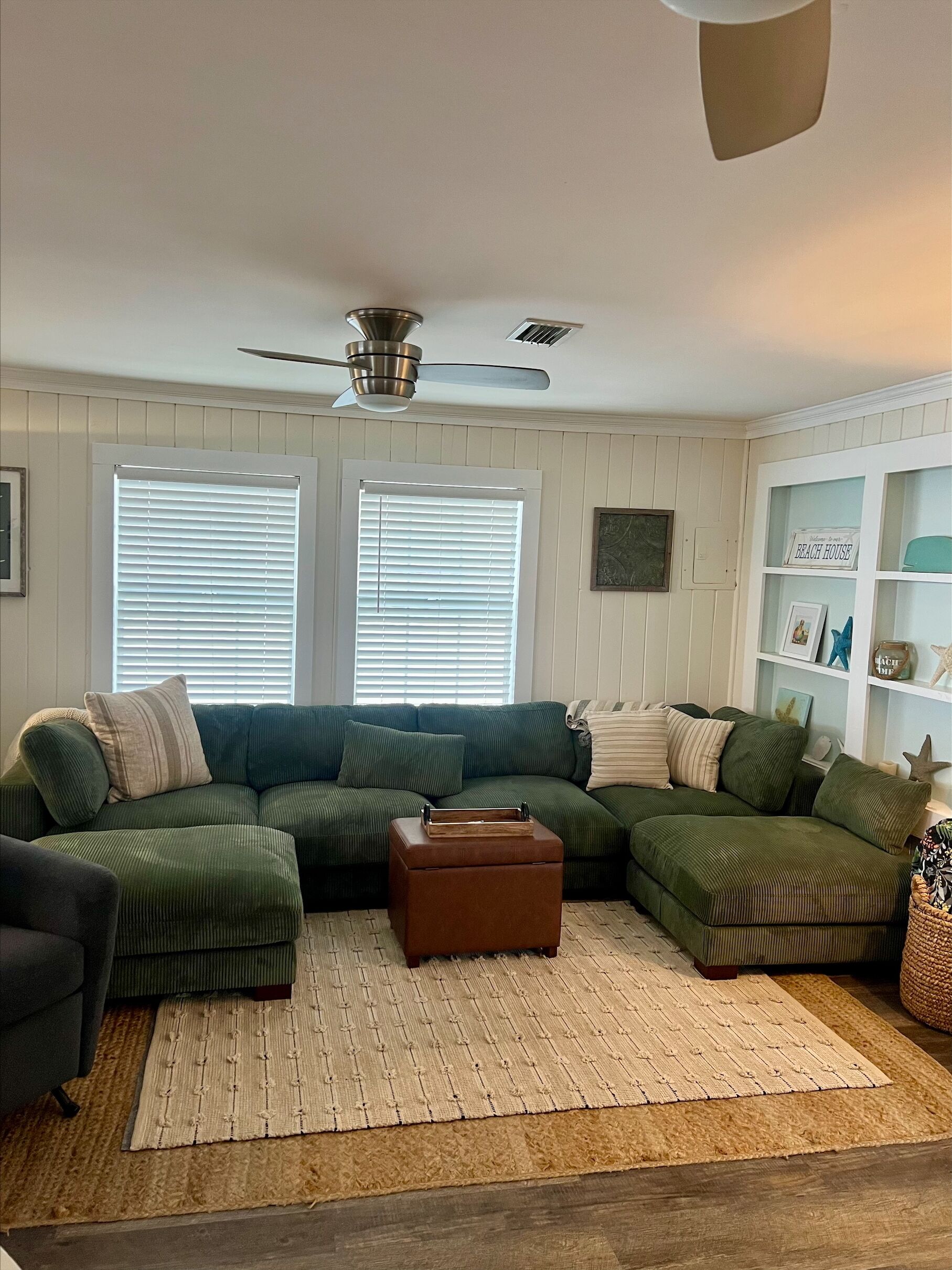 A living room with a sectional sofa, a ceiling fan, and a bookshelf.
