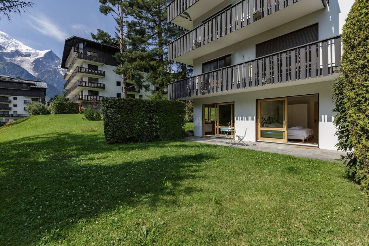 A modern multi-story building with balconies, a well-maintained lawn, and a mountain view in the background.