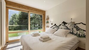 A bedroom with a large window, a bed with white linens, and a mountain-themed wall mural. - Modern 2BR | MtBlanc View | Terrace | Brevent 3mn (Chamonix-Mont-Blanc)