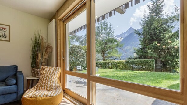 A room with a large window, a blue sofa, a patterned bean bag chair, and a potted plant. - Modern 2BR | MtBlanc View | Terrace | Brevent 3mn (Chamonix-Mont-Blanc)