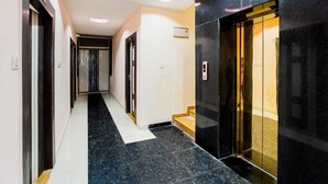 Un pasillo moderno con pisos de baldosas blanco y negro, un banco de madera y una puerta de ascensor de vidrio.