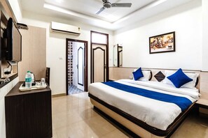 Quarto de hotel com cama, mesa de cabeceira, televisão, garrafa de água e um quadro na parede.