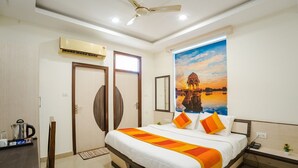 Una habitación de hotel con cama, ventilador de techo, aire acondicionado, cafetera y televisor montado en la pared.
