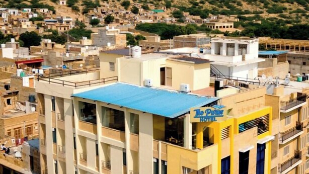 Un hotel con varios pisos y balcones, rodeado de una zona urbana densamente poblada y edificios diversos.