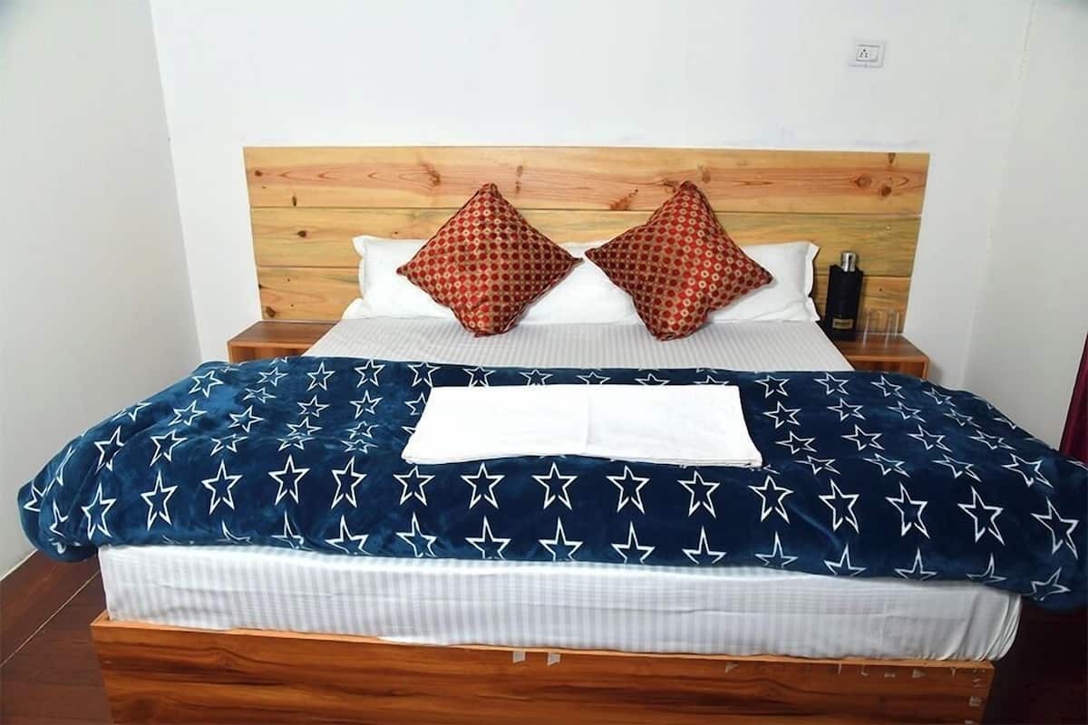A bed with a wooden headboard, two red patterned pillows, a white pillow, and a blue blanket with white stars.