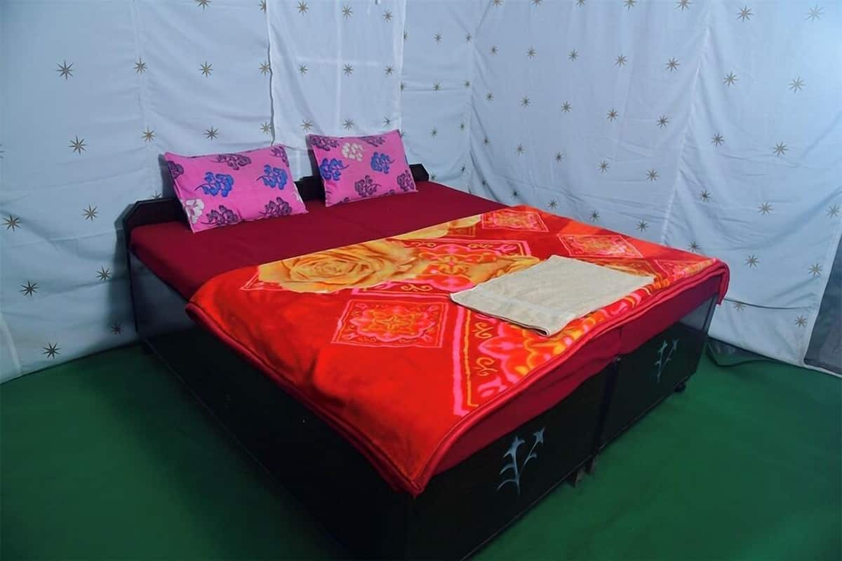 A bed with a red and orange patterned bedspread, two pillows with floral designs, and a white pillow. The bed is on a dark-colored frame.