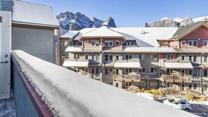 A hotel with multiple balconies, a snow-covered roof, and a mountain backdrop. - Penthouse•King Beds•Pool•BikeStorage (Canmore)