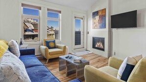 A modern living room with a sofa, armchairs, a coffee table, a fireplace, and large windows with a mountain view. - Penthouse•King Beds•Pool•BikeStorage (Canmore)