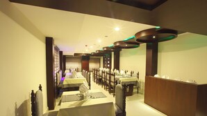 A dining area with tables set for service, a reception desk, and a modern ceiling design.