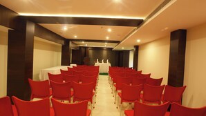 A conference room with rows of red chairs facing a white table at the front.