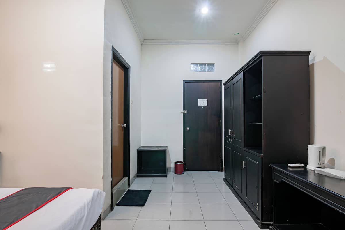 Habitación de hotel con cama, armario, mesita con tetera y cubo de basura.