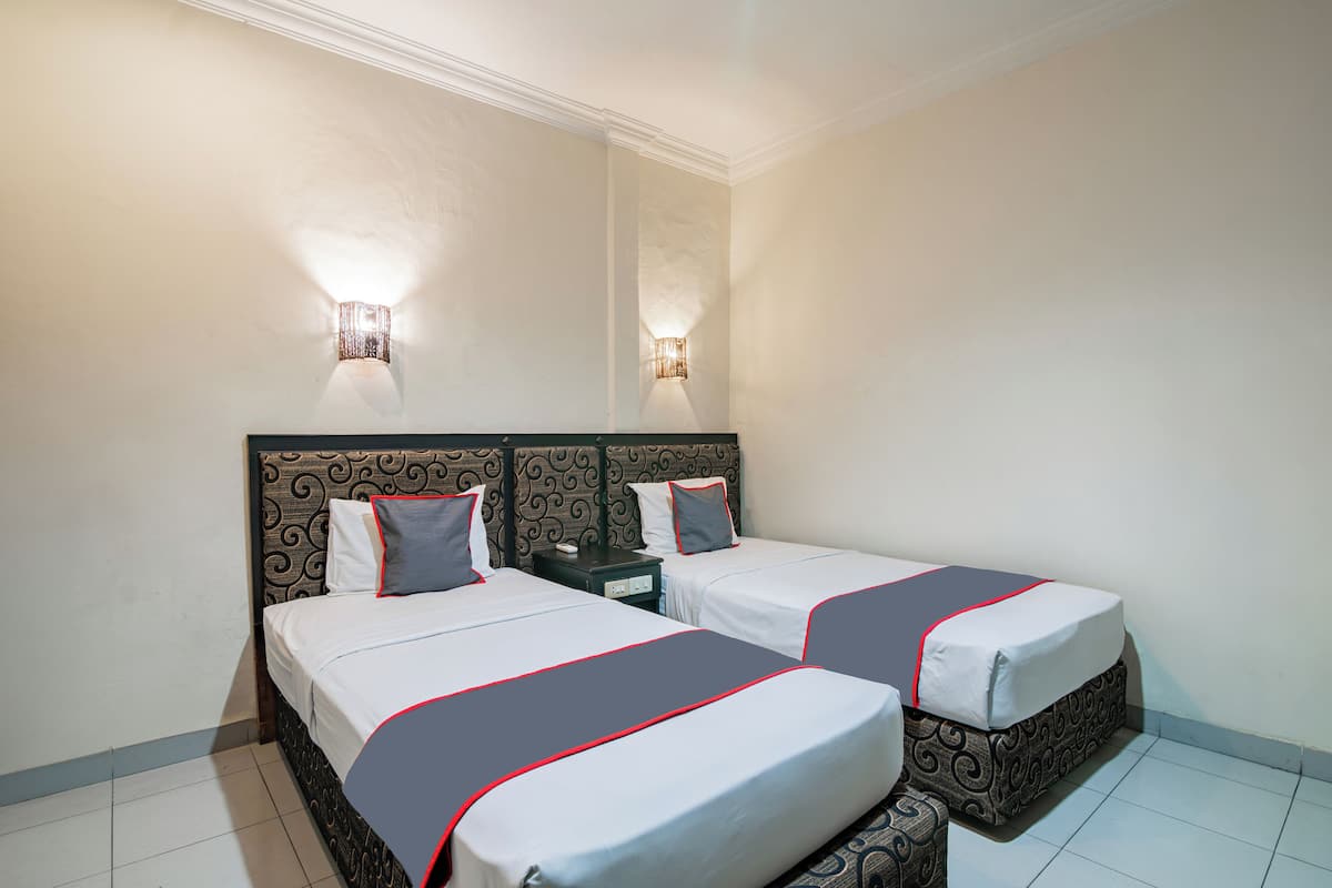 Habitación de hotel con dos camas, cada una con cabecero estampado, ropa de cama blanca con detalles rojos y dos lámparas fijadas a la pared.