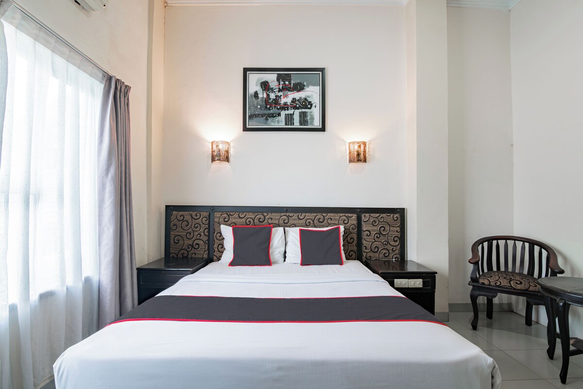 Habitación de hotel con una cama grande, dos mesitas de noche, una silla, un cuadro en la pared y dos apliques.