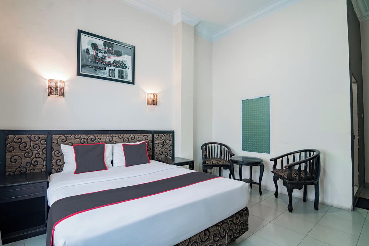 Habitación de hotel con una cama grande, dos mesitas de noche, una silla, una pequeña mesa y un cuadro colgado en la pared.