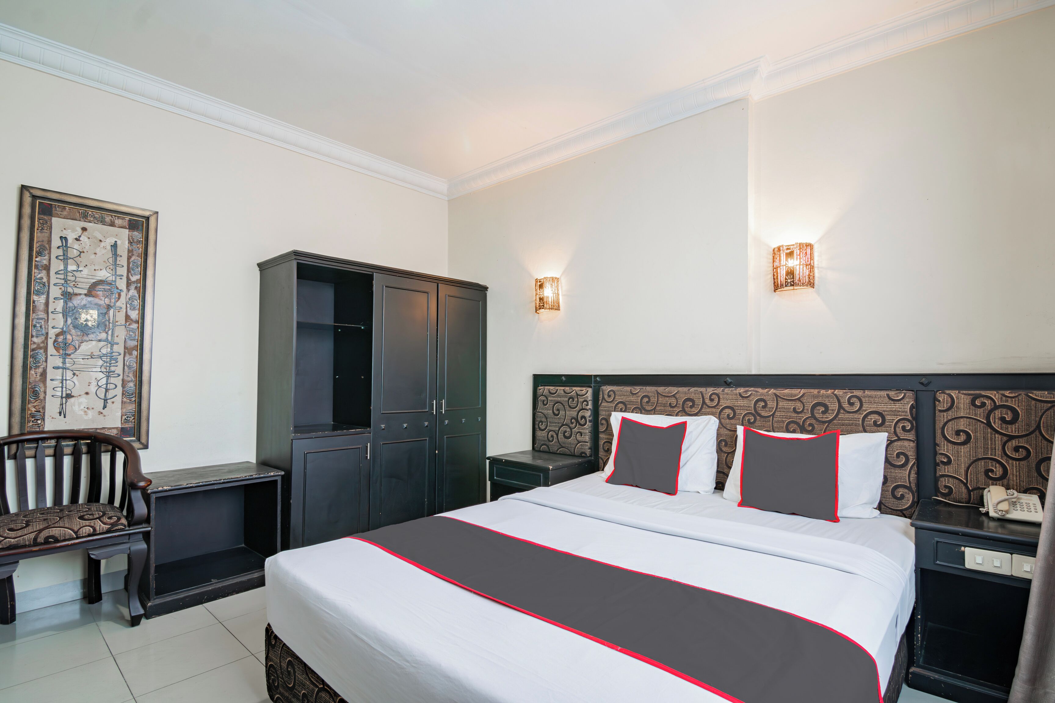 A hotel room with a large bed, a wardrobe, a desk, and two wall-mounted lights.