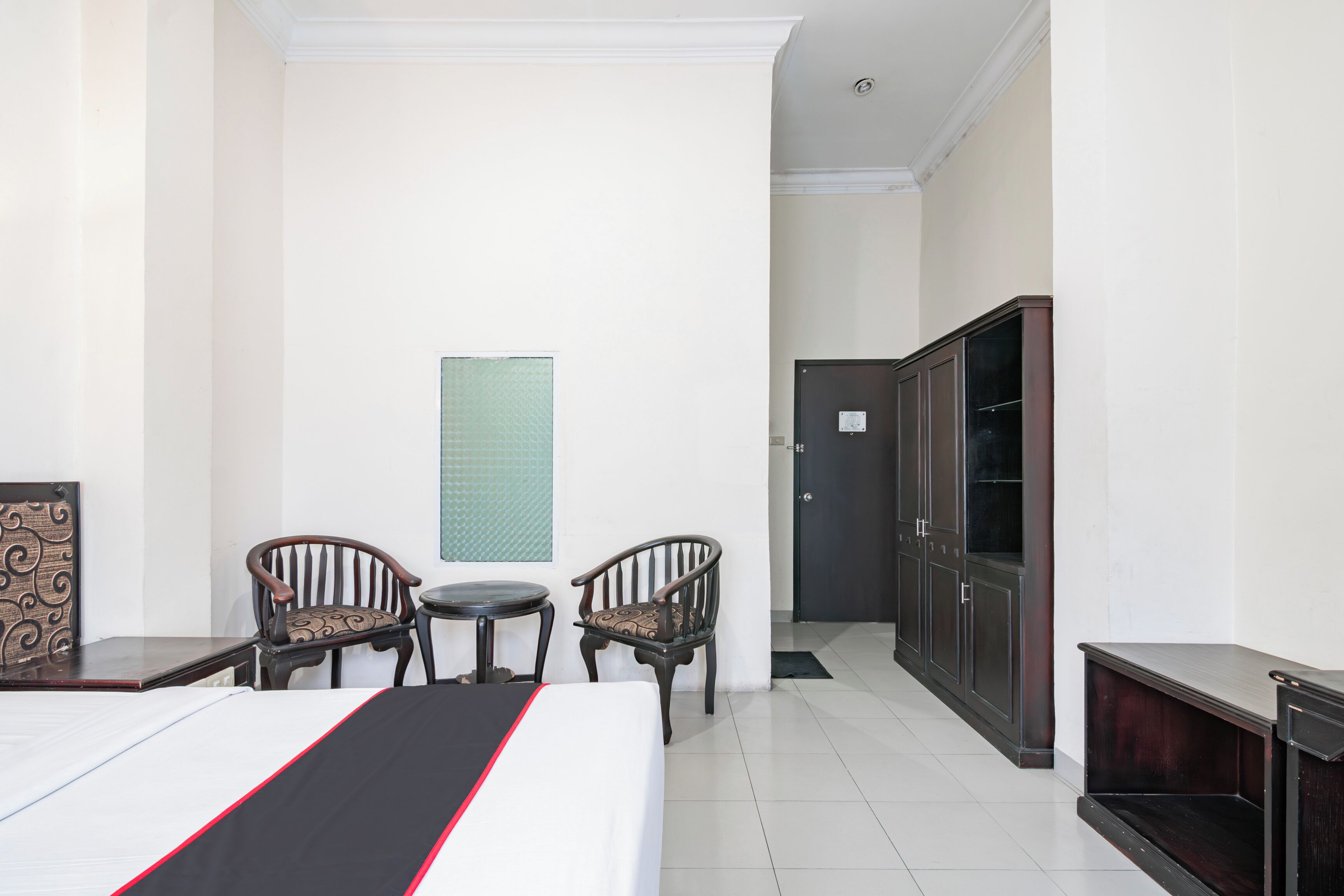 A hotel room with a bed, two chairs, a small table, a cabinet, and a door.