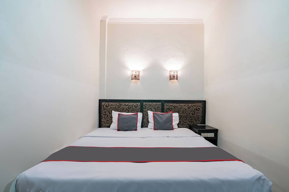 Habitación de hotel con una cama bien hecha, dos lámparas fijadas a la pared y una mesita de noche con una pequeña tabla.