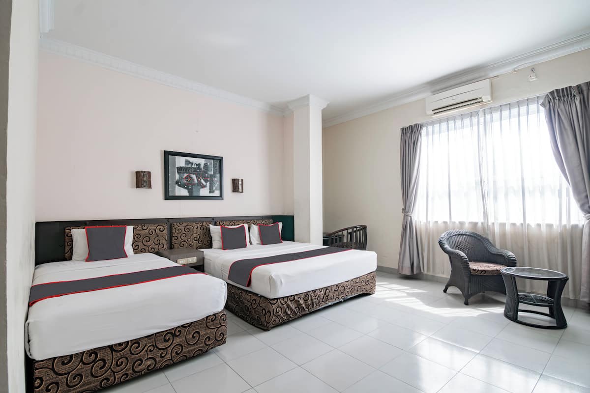 Habitación de hotel con dos camas, una silla, una mesa y un cuadro en la pared.