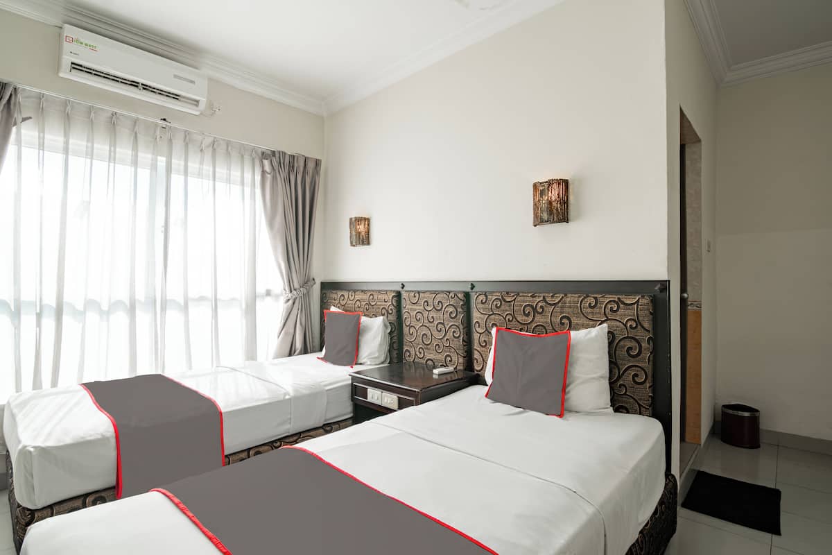 Habitación de hotel con dos camas individuales, una cama grande, un equipo de aire acondicionado, una mesita de noche, una lámpara y un cesto de basura.