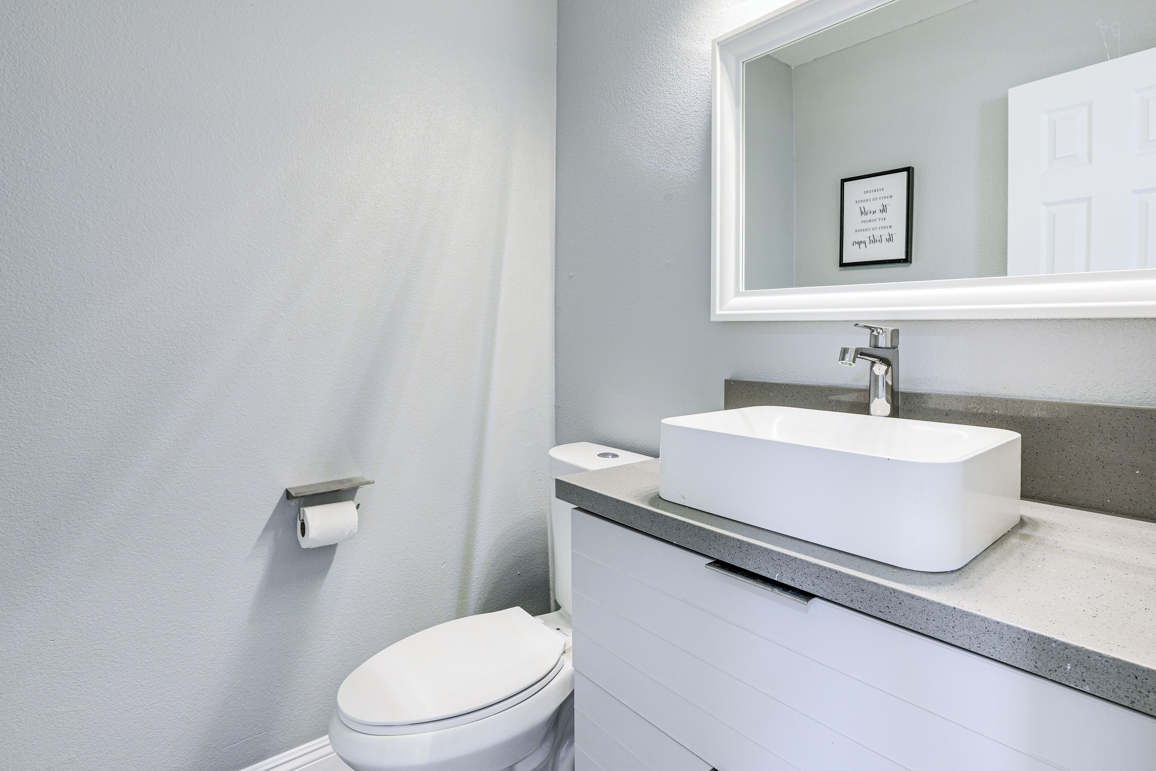 Un baño moderno con un inodoro blanco, un lavabo rectangular y un espejo sobre él.