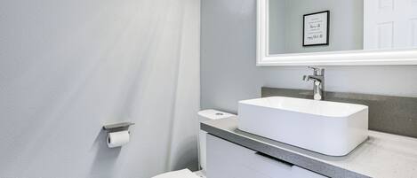 Un baño moderno con un inodoro blanco, un lavabo rectangular y un espejo sobre él.