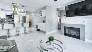 Une cuisine moderne équipée d’un four à micro-ondes, d’un réfrigérateur et de tabourets de bar. On y trouve également un espace salon avec une table basse en verre et une cheminée.